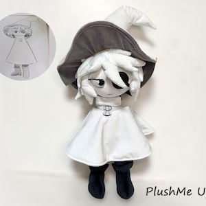 K&ouml;nnte beinhalten: Eine Pl&uuml;schpuppe einer Figur mit wei&szlig;en Haaren, einem wei&szlig;en Kleid und schwarzen Stiefeln. Die Puppe tr&auml;gt einen grauen Hut und hat ein Auge offen. Eine Skizze der Figur befindet sich in einem Kreis oben links. Der Text "PlushMe Up!" steht unten rechts.