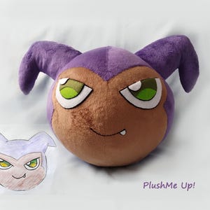May include: A plush toy in the shape of a cartoon character's head, featuring a purple head and ears, brown face, and green-eyed expression. A smaller sketch of the character is next to the plush. The text "PlushMe Up!" is in the lower right corner.