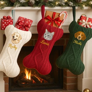 Op de afbeelding: Drie kerstsokken in de vorm van hondenbotten hangen aan een schoorsteenmantel. Eén is wit met een golden retriever en de naam "Rocky", één is rood met een kat en de naam "Luna", en één is groen met een beagle en de naam "Mochi".