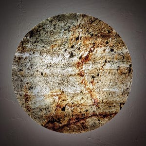 Può includere: Superficie circolare e strutturata con un aspetto naturale e terroso. La superficie presenta un mix di tonalità marroni, beige e bianche, con un motivo ruvido e organico che ricorda la pietra o le venature del legno. L'effetto complessivo è una miscela di colori e texture naturali.