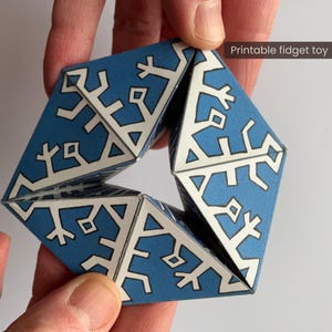Könnte beinhalten: Ein blau-weißes geometrisches Zappelspielzeug, das von Händen gehalten wird. Das Spielzeug besteht aus gefaltetem Papier und weist ein sich wiederholendes Muster aus weißen Formen auf blauem Hintergrund auf. Der Text auf dem Bild lautet "Printable fidget toy".