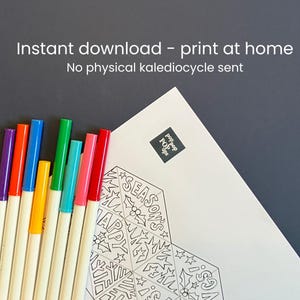 May include: A white paper sheet featuring a black and white line art design with the text "SEASON'S HAPPY GREETINGS" and holly illustrations, accompanied by eight colorful felt-tip markers in purple, orange, blue, yellow, green, teal, pink, and red.
