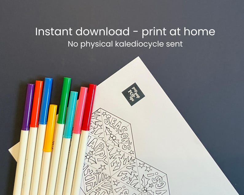 May include: A white paper sheet featuring a black and white line art design with the text "SEASON'S HAPPY GREETINGS" and holly illustrations, accompanied by eight colorful felt-tip markers in purple, orange, blue, yellow, green, teal, pink, and red.