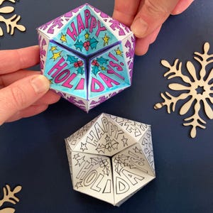 Two printable paper kaleidocycles. The visible face of each shows hand drawn decorations and the words 'Happy Holidays!' One has been printed in black and white ready to be coloured-in and the other has been coloured so that the background is blue.