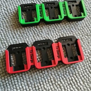 May include: A selection of black plastic battery holders with coloured accents. Three green holders with "Full Charge" text and three red holders with "To Charge" text are visible. The holders are on a grey, textured surface.