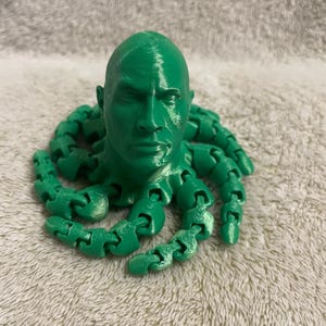 May include: A green 3D printed sculpture of a person's head with multiple tentacles coming out of the back of the head.