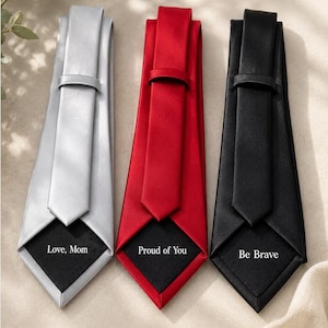May include: Three silk ties in silver, red, and black, each with a contrasting black tip. The silver tie reads "Love, Mom," the red tie says "Proud of You," and the black tie says "Be Brave."