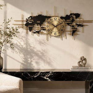 May include: A large horizontal wall clock featuring a gold circular face with black numerals and hands. The clock is mounted on a gold metal grid structure shaped like a world map with black continents, including labels for Europe, Asia, Africa, Oceania, North America, and South America, plus two small black airplane silhouettes.