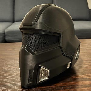 Peut inclure: Un casque noir avec une visière en maille et une surface texturée. Le casque a un accent argenté sur le côté.