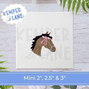 Pode incluir: Design de cabeça de cavalo bordada com laço rosa e freio azul em fundo branco. O texto "Kemper Lane" está em um círculo azul claro. O texto "Mini 2", 2.5" & 3"" está em uma faixa azul.