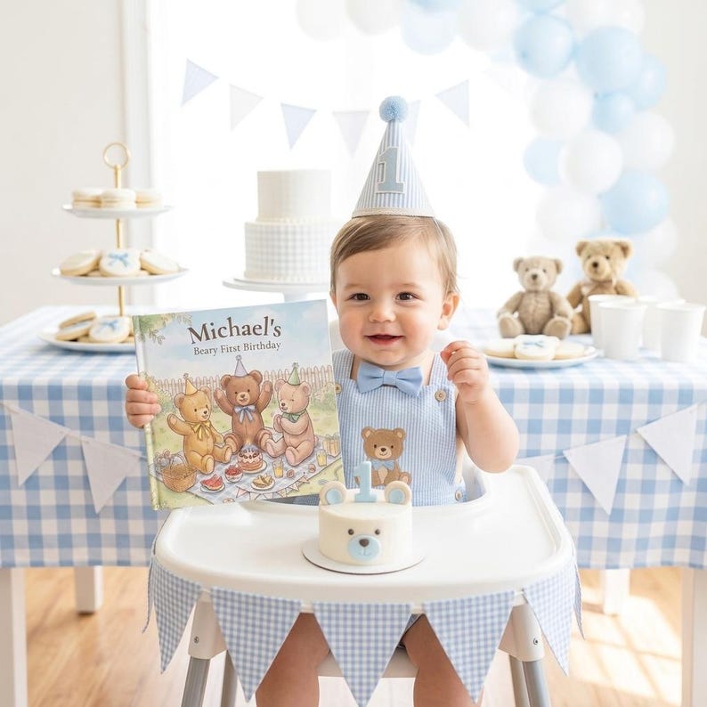May include: A child wearing a light blue pinstriped romper with a matching bow tie and a party hat with the number one. The child holds a book titled Michael's Beary First Birthday, sitting in a high chair with a small bear-themed cake.
