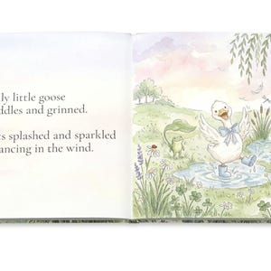 May include: An open book with watercolor illustrations. The right page shows a white goose in blue boots splashing in a puddle, with a frog and other details. Text on the left page reads: "That silly little goose saw puddles and grinned. Droplets splashed and sparkled while dancing in the wind."