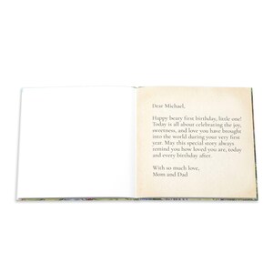 May include: An open book with a blank white left page and a right page featuring a printed message that reads: Dear Michael, Happy beary first birthday, little one! Today is all about celebrating the joy, sweetness, and love you have brought into the world during your very first year. May this special story always remind you how loved you are, today and every birthday after. With so much love, Mom and Dad.