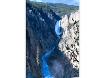 May include: A scenic photograph of a waterfall cascading into a river within a deep canyon. The water is a vibrant blue, contrasting with the brown and gray canyon walls. Lush green trees line the canyon rim under a blue sky.