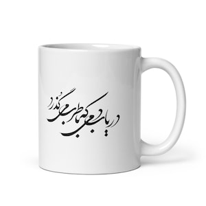 May include: A white ceramic mug featuring black Persian calligraphy printed on the front. The mug has a cylindrical body with a smooth finish and a curved handle on the right side. The black script is centered and clearly visible against the white.