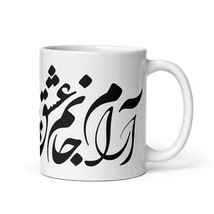 Puede incluir: Una taza de cerámica blanca con caligrafía persa negra impresa en el frente. La taza tiene un acabado liso y brillante, un cuerpo cilíndrico y un asa curva en el lado derecho. La escritura negra es audaz, fluida y está orientada verticalmente.
