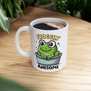 May include: A white ceramic mug with a black handle and the text "But First, Coffee" in a black, bold font. The mug is sitting on a wooden surface. The mug is 4 inches tall.