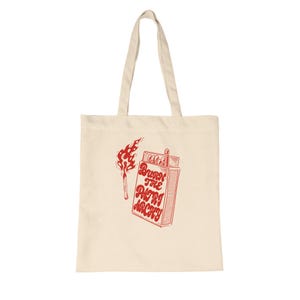 Könnte beinhalten: Cremefarbene Tragetasche mit roter Grafik eines brennenden Streichholzes und einer Streichholzschachtel mit dem Text "Burn the Patriarchy". Die Tasche hat zwei Griffe und ist aus einem weichen, strapazierfähigen Stoff gefertigt.