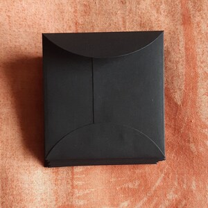 May include: A stack of black square envelopes with rounded corners. The envelopes are made of a thick, sturdy paper.