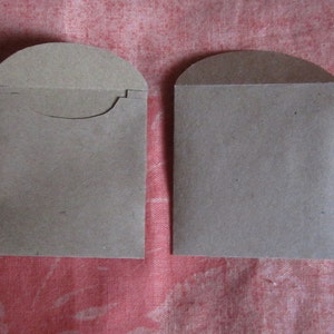 May include: Two brown paper envelopes with rounded tops. The envelopes are blank and have a flap on the top.