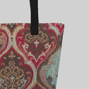 Könnte beinhalten: Tragetasche mit einem detaillierten, verzierten Muster in Rot-, Braun- und Blautönen. Die Tasche hat einen schwarzen Riemen und ein dekoratives Design im Vintage-Stil.