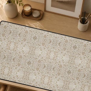 May include: A rectangular desk mat featuring a repeating beige and cream floral pattern with a black border. The surface has a detailed, intricate design of small flowers and swirling motifs covering the entire top area of the mat.