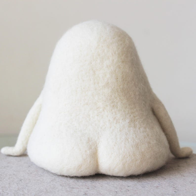 K&ouml;nnte beinhalten: Ein wei&szlig;es, flauschiges Filztier in Form eines Pinguins, das auf einer grauen Oberfl&auml;che sitzt. Das Spielzeug hat einen runden K&ouml;rper und einen kleinen Kopf mit einem spitzen Schnabel.