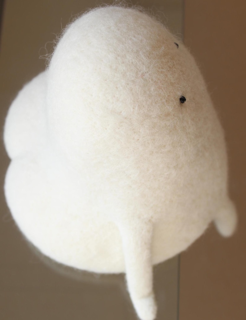 K&ouml;nnte beinhalten: Ein wei&szlig;es, flauschiges Filzspielzeug in Form einer Wolke mit zwei kleinen Armen. Das Spielzeug hat zwei schwarze Augen.