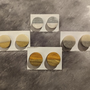 May include: Six pairs of round, half-circle earrings with a white top and a different colored bottom. The colors are gold, silver, and gray.