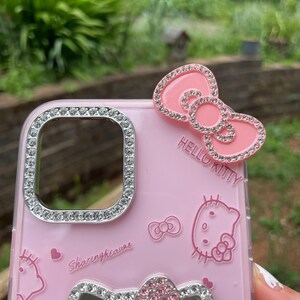 Pu&ograve; includere: Custodia per telefono rosa con un design di Hello Kitty. La custodia presenta un fiocco con strass e le parole "Hello Kitty". L'obiettivo della fotocamera e il fiocco inferiore sono anch'essi decorati con strass. La custodia ha le parole "Sharingheaves".