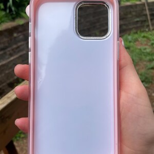 Pu&ograve; includere: Una custodia trasparente per telefono con bordo rosa. La custodia ha un ritaglio argentato per la fotocamera e un retro trasparente. La custodia del telefono &egrave; tenuta in mano da una persona.