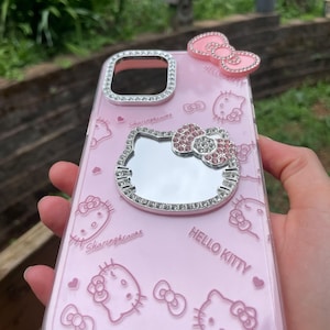 Pu&ograve; includere: Custodia per telefono Hello Kitty rosa con specchio e fiocchi. La custodia ha un bordo trasparente con finiture in strass argentati attorno alla fotocamera e allo specchio. La custodia ha le parole "Hello Kitty" e "Autumn".