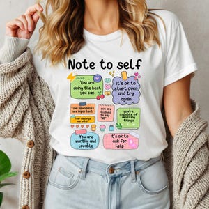 May include: White t-shirt with a colorful design that says "Note to self" and includes positive affirmations like "You are doing the best you can" and "It's ok to start over and try again".