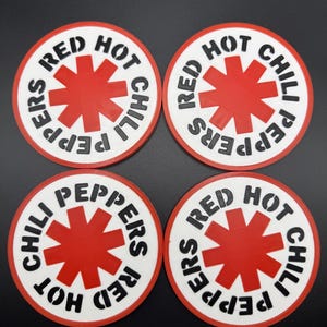 Puede incluir: Cuatro posavasos redondos con borde blanco y diseño de estrella roja en el centro. Las palabras "RED HOT CHILI PEPPERS" están impresas en negro alrededor del borde de cada posavasos. Los posavasos están sobre una superficie negra.