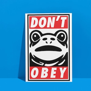 May include: A rectangular white print with a black border, featuring a stylized frog face. The words "DON'T" and "OBEY" are in bold white letters on red rectangular backgrounds, above and below the frog illustration.
