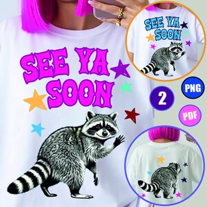 May include: A white t-shirt featuring a graphic of a raccoon waving its paw. Above the raccoon, the text reads SEE YA SOON in large purple letters. The design includes several colourful stars in yellow, blue, purple, and red scattered around.