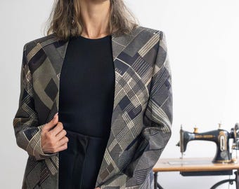May include: A geometric patterned blazer in shades of grey, black, and tan. The jacket is worn over a black top and trousers. A vintage sewing machine is visible in the background.