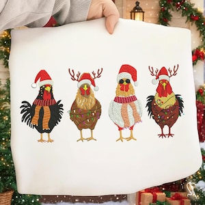 Puede incluir: Una funda de almohada blanca con cuatro gallinas bordadas vestidas para Navidad. Cada gallina lleva un gorro de Papá Noel, y algunas tienen bufandas, cornamentas o gafas de sol. Las gallinas están decoradas con luces navideñas.