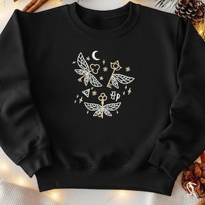 May include: Black sweatshirt featuring a gold design of keys with wings, stars, a moon, and the letters "HP". The design is centered on the chest. The sweatshirt is a crew neck style.