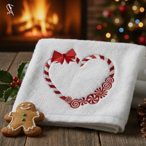 May include: White Christmas-themed hand towel with a candy cane heart design and a red bow. The heart is outlined with red and white stripes and surrounded by embroidered peppermint candies. A gingerbread man cookie is on the wooden surface.
