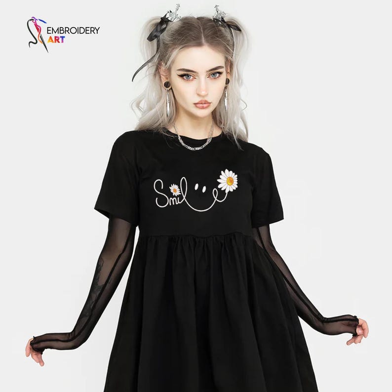 May include: Black short-sleeved dress with a white daisy and the word "Smile" in script. The dress has a gathered skirt and is paired with sheer black arm sleeves. The image also shows a logo for "Embroidery Art".