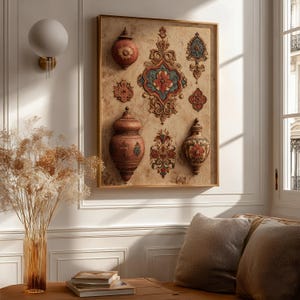 May include: A framed wall art piece featuring a beige background with several ornate, three-dimensional designs and decorative vases in shades of red, brown, and blue. The artwork is displayed on a white wall, with a vase of dried flowers and a table in the foreground.
