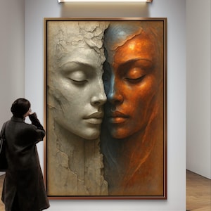 Może przedstawiać: Oprawione dzieło sztuki przedstawiające dwie twarze, jedną w skali szarości, a drugą w ciepłych odcieniach pomarańczu, podzielone na pół. Twarze są spokojne, z zamkniętymi oczami. Osoba w ciemnym płaszczu stoi przed dziełem w galerii.