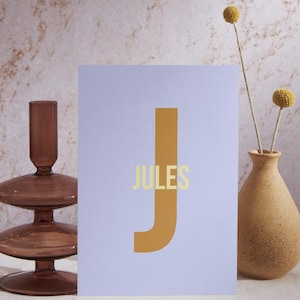 May include: A light purple card with a large, mustard yellow letter "J" and the word "JULES" in a light yellow font.