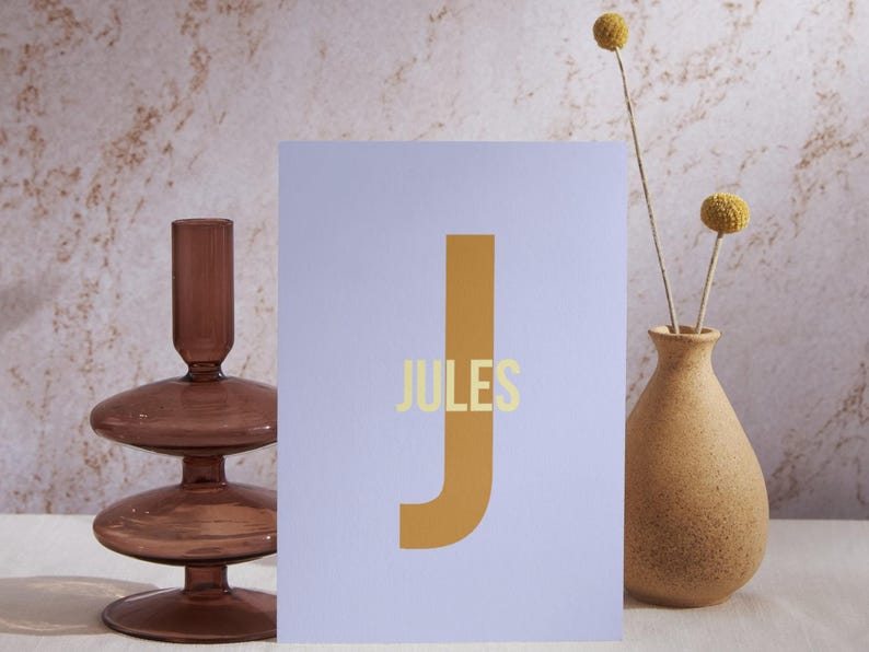 May include: A light purple card with a large, mustard yellow letter "J" and the word "JULES" in a light yellow font.