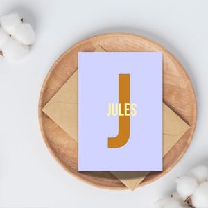 May include: A light blue card with a large brown letter "J" and the word "JULES" in yellow letters.
