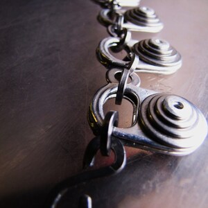 May include: A silver chain necklace with multiple circular pendant charms. Each charm is made of stacked metal rings, creating a layered effect.