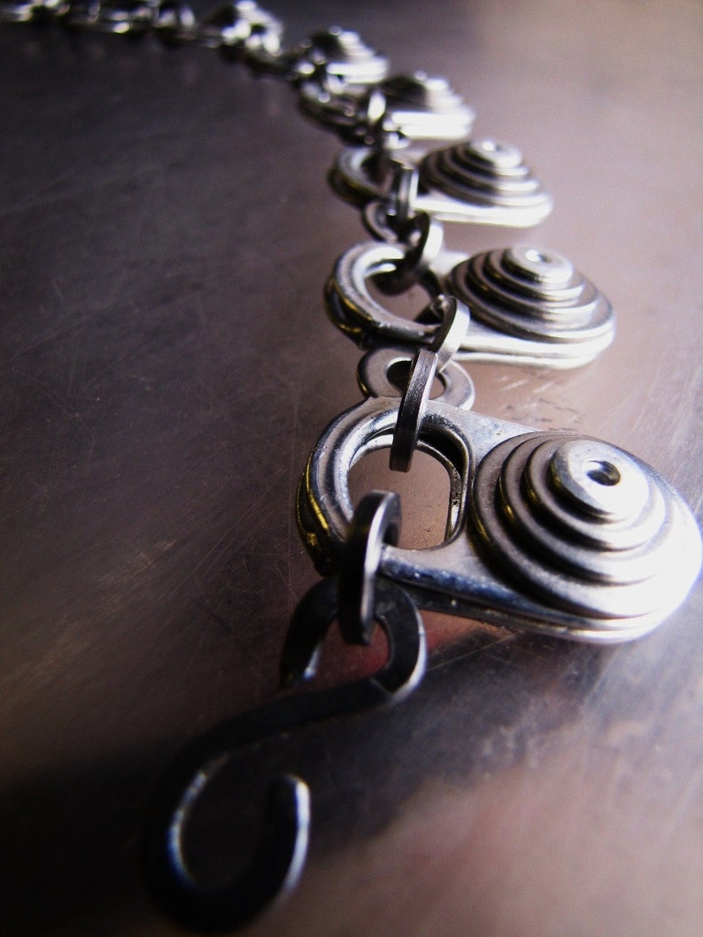May include: A silver chain necklace with multiple circular pendant charms. Each charm is made of stacked metal rings, creating a layered effect.