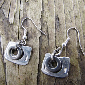 May include: A pair of silver earrings with a unique design featuring a small circle and a larger, irregular shape. The earrings are made of metal and have a simple, modern look.