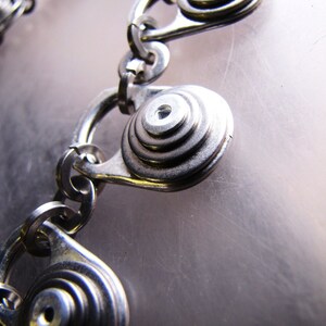 May include: A silver chain bracelet with multiple circular charms. Each charm is made of stacked metal rings, creating a layered effect.